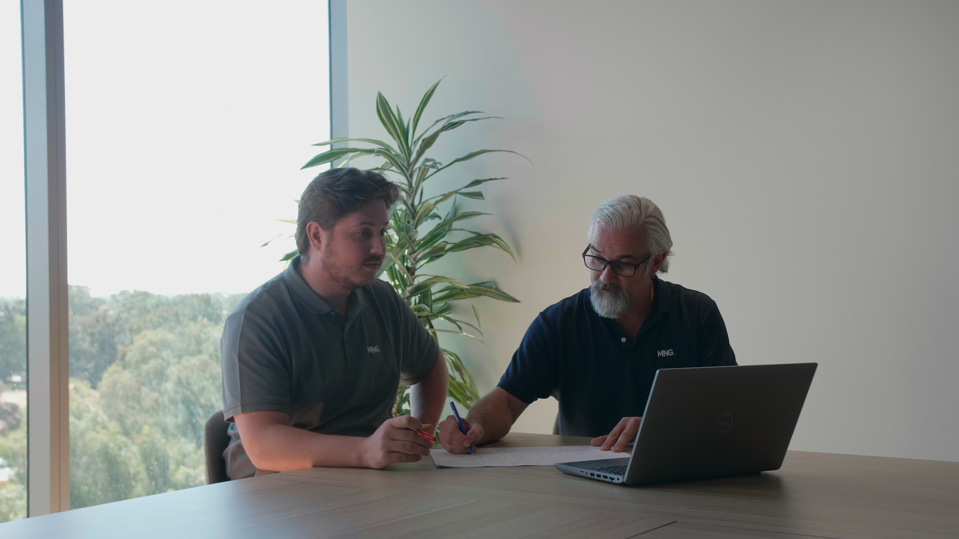 Two MNG planners collaborating at a desk with laptop and documents