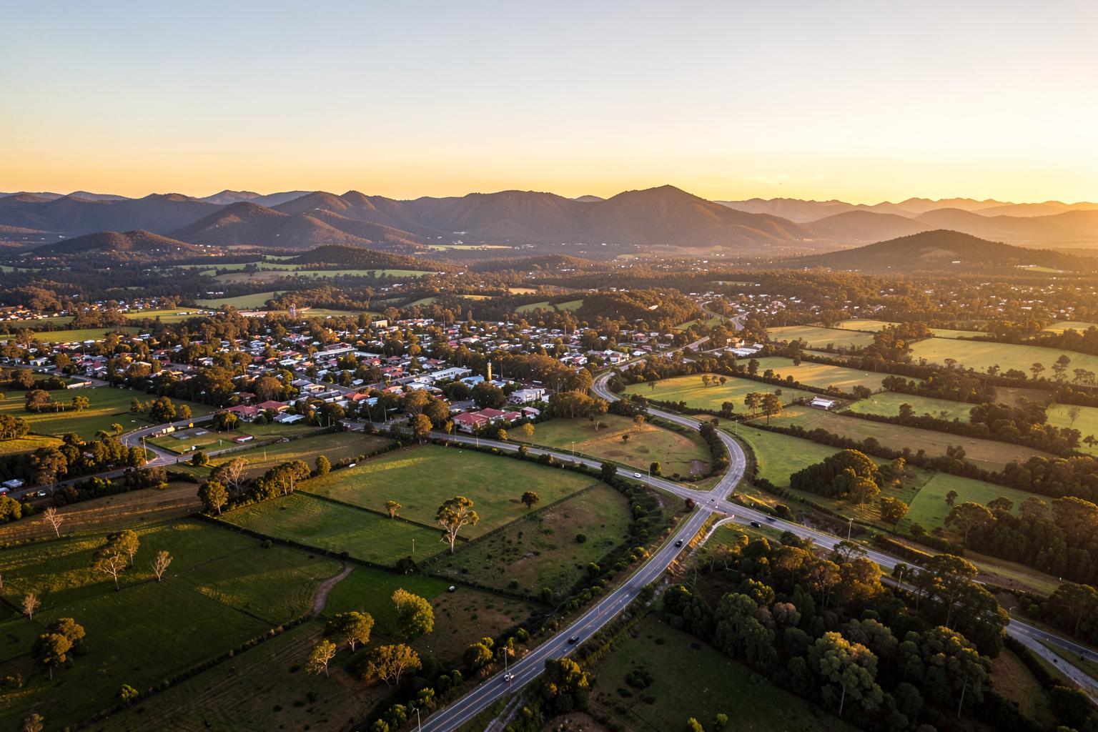 Aerial view of a regional Queensland town, farmland and distant ranges at golden hour